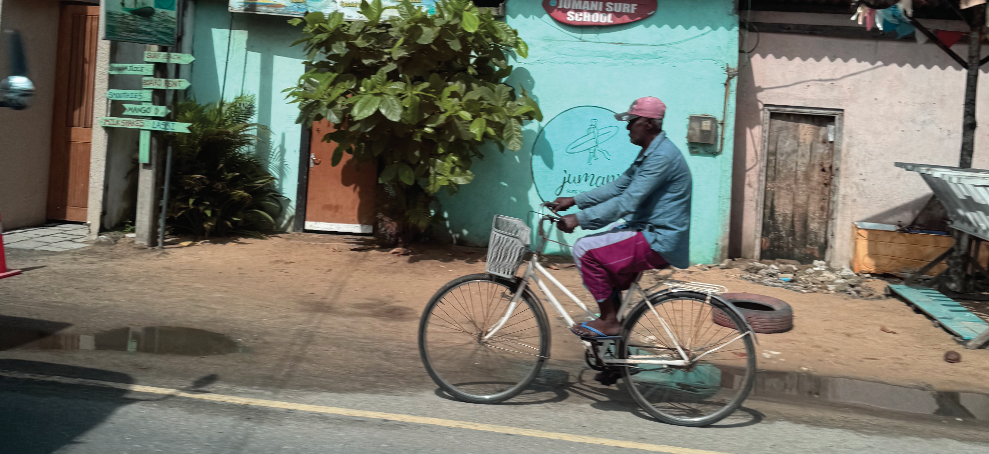 Sri Lankan local riding a bicycle on a street with a colorful building in the background.