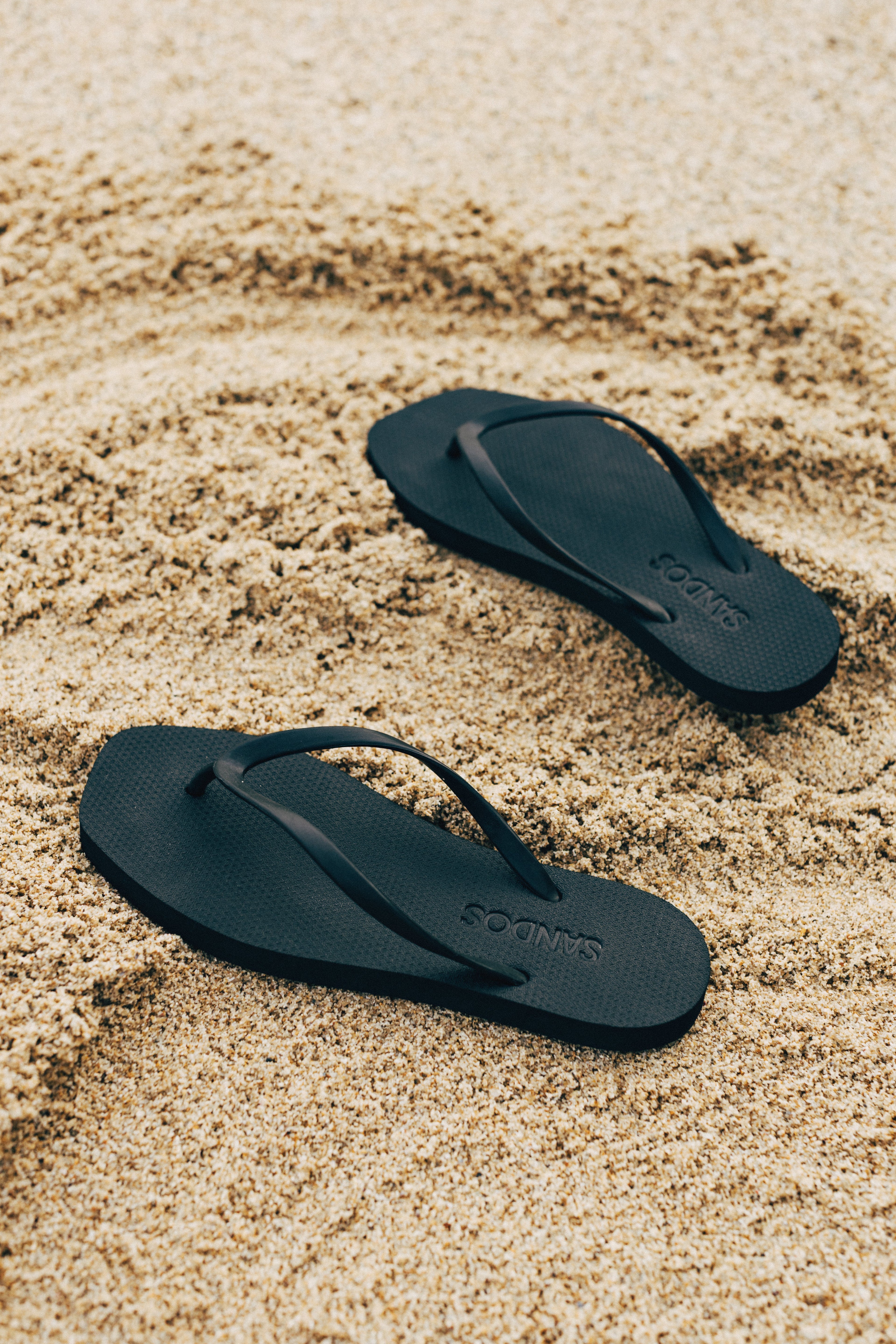 A model wearing a pair of Black Sandos flip flops at a table