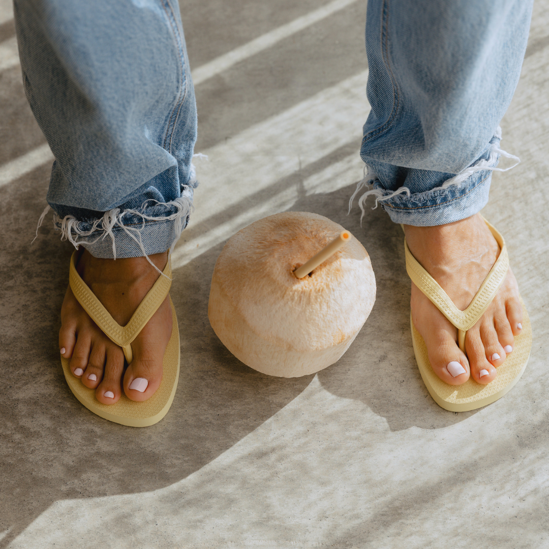 Person wearing limoncello Sandos flip flops with a coconut on a stone surface