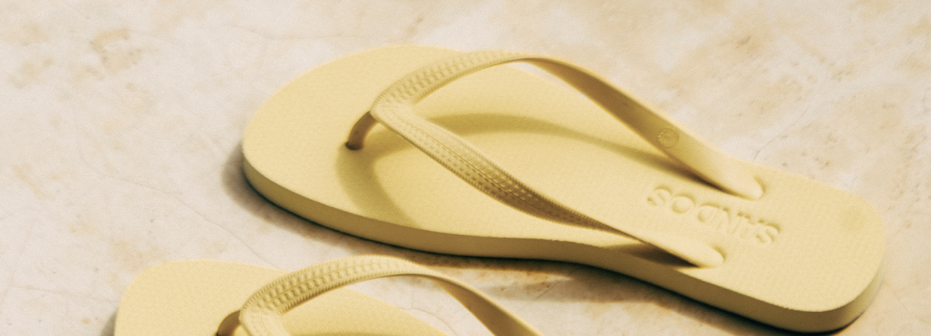 Pair of Limoncello Sandos flip-flops on a sandy background